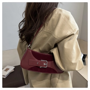 Close-up of burgundy suede shoulder bag with metal buckle on a khaki coat model