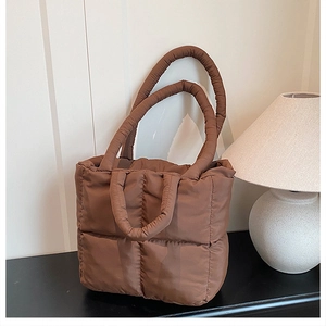 Detail of a brown quilted puffer tote bag with dual handles for shoulder and hand carry