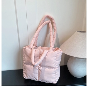 Detail of pink quilted puffer tote bag with four handles on a minimalist table