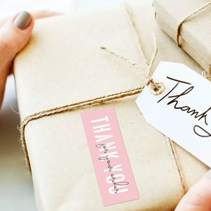 Pink rectangular Thank You stickers and white tags on a brown craft gift box