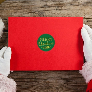 Merry Christmas green and gold foil sticker on red card held by Santa hand
