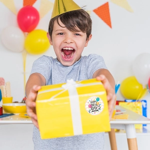 Boy handing a yellow birthday gift box with a Happy Birthday sticker and balloons