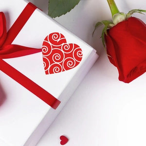 Red heart-shaped stickers with white spiral patterns on a gift box with a red rose