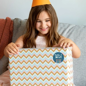 Round Make a Wish birthday sticker on gift box with girl in party hat background