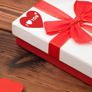 Valentine's Day gift box with red ribbon and I Love You heart sticker on wooden table