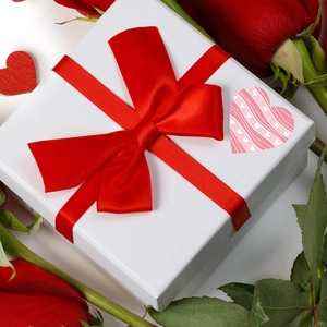 Valentine's Day heart stickers with pink waves on a gift box with red ribbon and roses