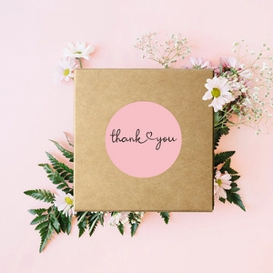Pink round Thank You stickers with heart design on a kraft gift box with floral decor