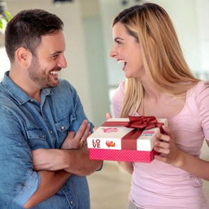 Coffret cadeau Saint-Valentin avec ruban rouge et motifs de cœurs tenu par un couple