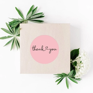 Pink round thank you sticker on kraft gift box with floral and green leaf accents