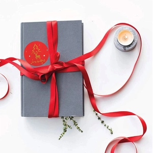 Close-up of red Merry Christmas stickers with golden reindeer on gift-wrapped notebook