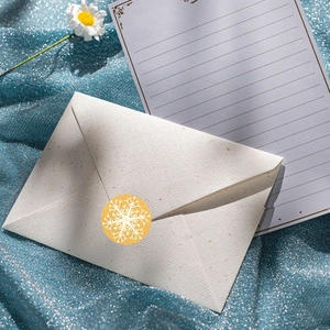 White textured Christmas envelope with golden snowflake sticker on blue glitter backdrop
