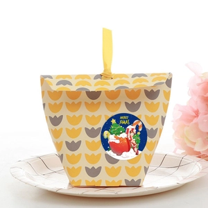 Roll of Merry Christmas kraft stickers on a patterned gift box with yellow ribbon handle