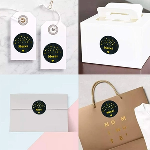 Roll of black and gold Merci stickers for gift packaging, featuring gold foil lettering