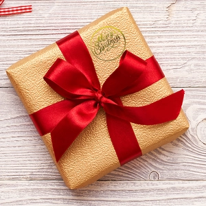 Transparent gold foil Merry Christmas stickers on a gift box with a red satin ribbon