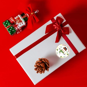 Macro view of Christmas stickers with snowmen and holly on white textured gift box