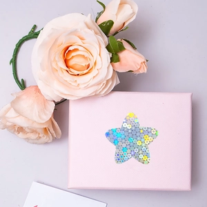 Pink woven texture gift box with star cutout and colorful laser sequins on a grey background