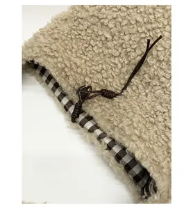 Detail of fuzzy beige sherpa bag with brown plaid lining and leather drawstring closure