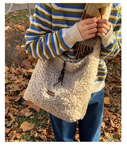 Close-up of fluffy cream fleece tote bag with brown leather tag in an autumn outdoor setting