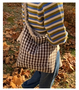 Detail of checkered tote bag featuring plush lamb wool lining and front pocket on grass
