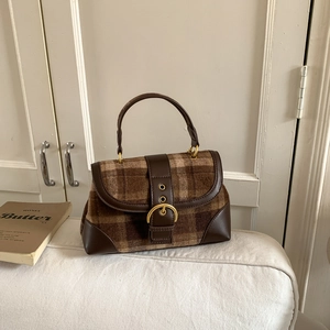 Close-up of retro brown plaid fabric and leather flap bag with large gold metal buckle