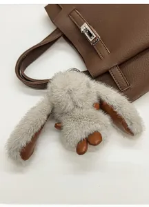 Gros plan d'un mignon pendentif lapin en peluche grise sur un sac seau en cuir marron