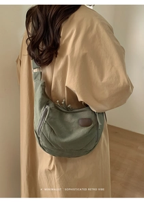 Sac hobo en toile vert foncé avec écusson en cuir porté par un mannequin dans un décor épuré