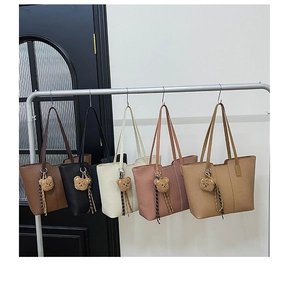Multi-color pebbled leather tote bags with cute bear charms hanging on a metal rack