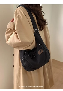 Vue détaillée d'un sac demi-lune noir minimaliste porté sur un trench-coat classique