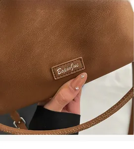 Detail of brown litchi pattern bucket bag featuring a stitched brand tag and woven strap