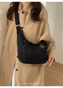 Détail du sac croissant en toile noire avec bandoulière large et étiquette en cuir