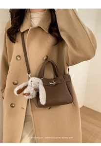 Detail of dark brown lychee leather bucket bag with metal buckle and plush rabbit charm