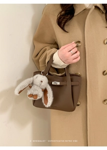 Detail of brown lychee leather bucket bag with silver lock and plush rabbit charm