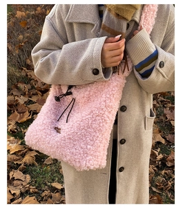 Close-up of pink fuzzy plush shoulder bag with black drawstring in an autumn setting