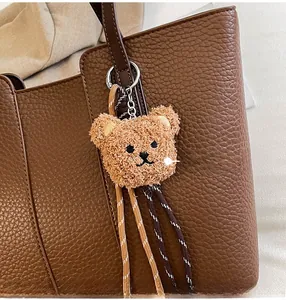 Detail of plush bear charm with woven rope on a textured brown leather tote bag