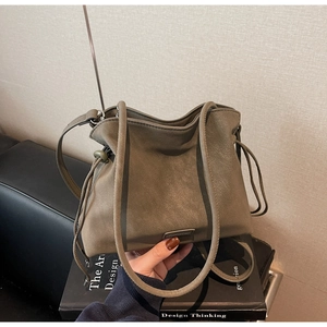 Detail of a matte leather drawstring bucket bag on a minimalist book stack backdrop