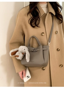 Détail d'un sac à main en cuir gris avec logo de marque et charm de lapin en peluche