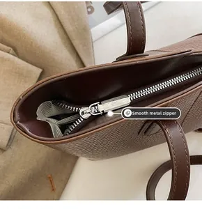 Detail of smooth silver hardware zipper and lychee pattern leather on brown tote bag