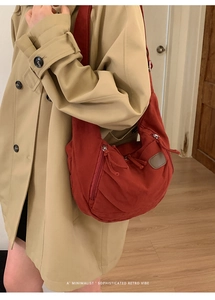Deep red crescent canvas tote bag with outer zipper pocket shown on a trench coat