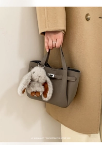 Detail of grey leather tote bag with silver twist lock and plush rabbit charm accessory