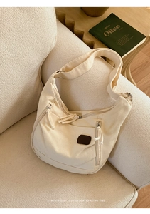 Détail d'un sac bandoulière en toile blanc cassé avec fermetures éclair sur un canapé beige