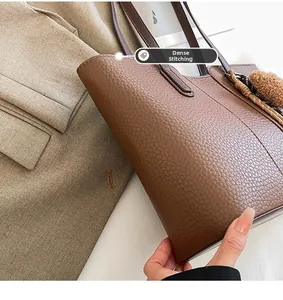 Close-up of precise stitching on textured brown leather tote bag with pompom charm