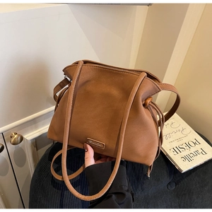 Detail shot of brown leather bucket bag with metal logo on corduroy background