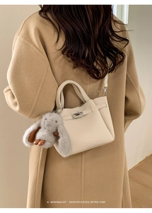 Detail of off-white leather handbag with plush charm on camel wool coat