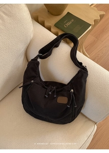 Détail du sac croissant en toile noire avec plusieurs poches zippées sur un canapé