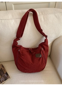 Détail du sac bandoulière rétro en toile bordeaux avec zips posé sur un canapé blanc