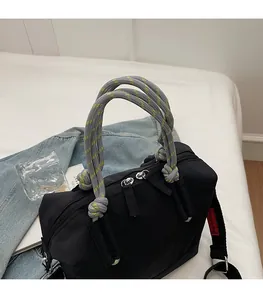 Détail du sac bandoulière noir avec poignée tressée grise et doubles zips métalliques