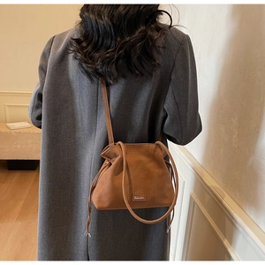 Brown matte leather bucket bag shown on a model from a back side view for scale