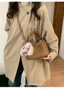 Brown litchi leather bucket bag with plush rabbit charm worn by model in trench coat