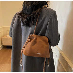 Detailed view of a retro brown pleated bucket bag worn by a model in a gray blazer