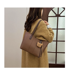 Detail of dark brown litchi grain leather tote bag featuring a cute plush bear pendant